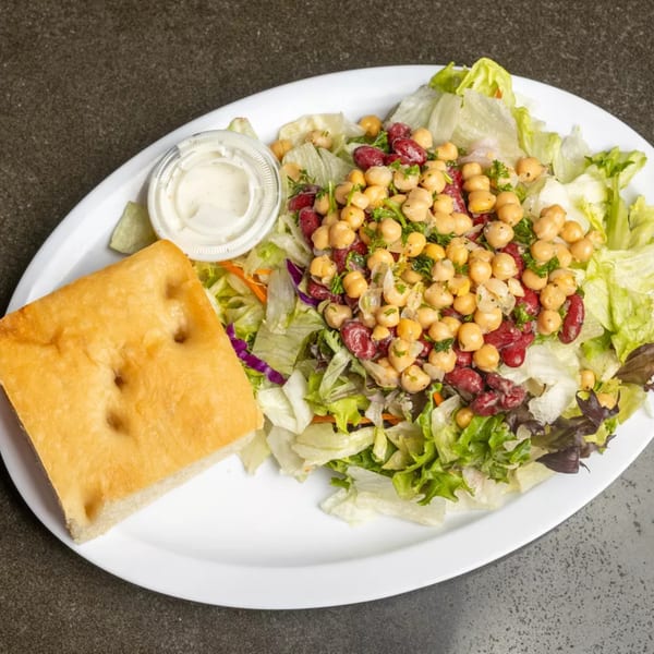 Fresh garden salad with chickpeas, kidney beans, and focaccia bread on a white plate.