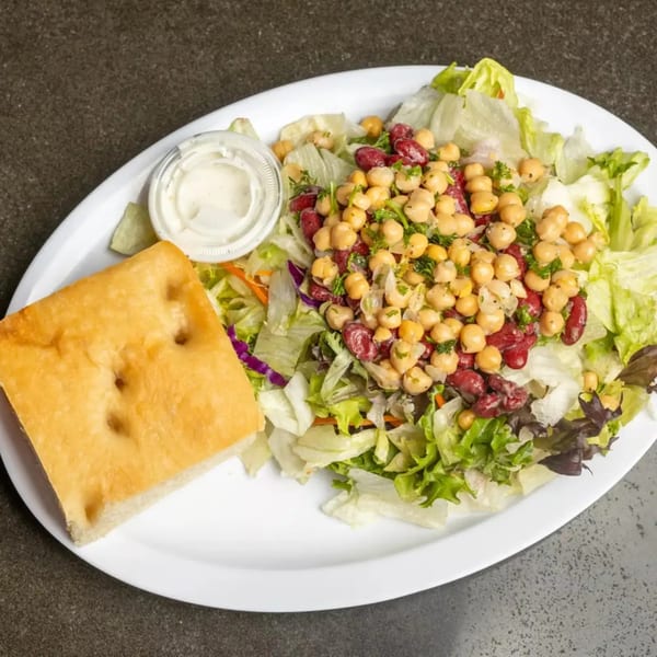 A fresh garden salad with chickpeas, kidney beans, and focaccia bread, served with a side of dressing.