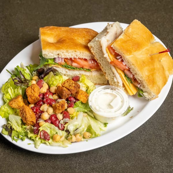 Focaccia sandwich with cheese, tomato, and lettuce, served with a bean salad and dressing.