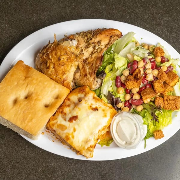 Roasted chicken, lasagna, focaccia bread, and a salad with beans and croutons on a white plate.