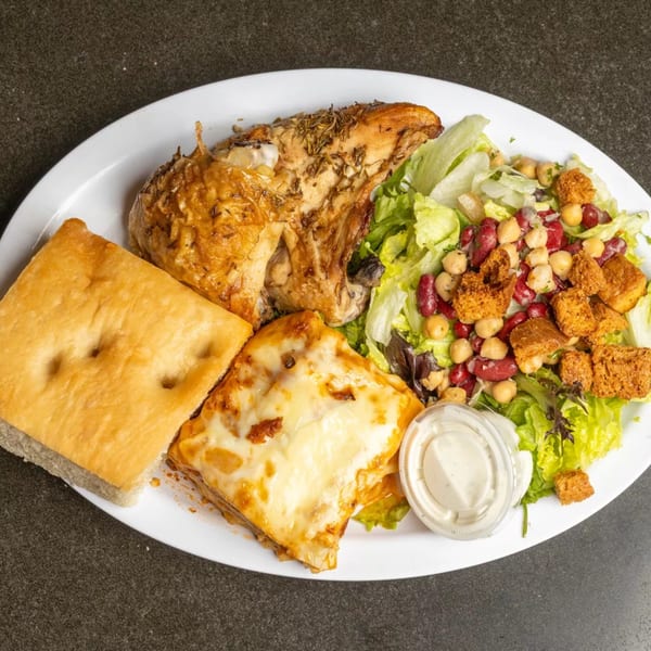A white plate with roasted chicken, lasagna, focaccia bread, and a salad with dressing.