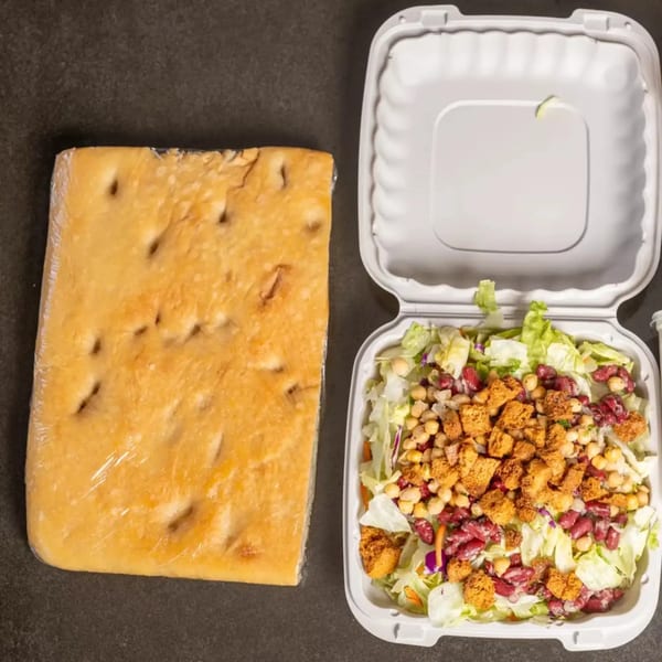 Focaccia bread and a takeout container with a salad topped with chickpeas, kidney beans, and croutons.