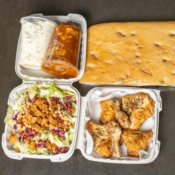 Takeout meal with roasted chicken, salad, focaccia bread, and two containers of sauces.